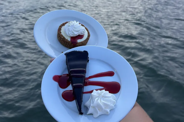Two desserts on plates held above a lake at sunset.