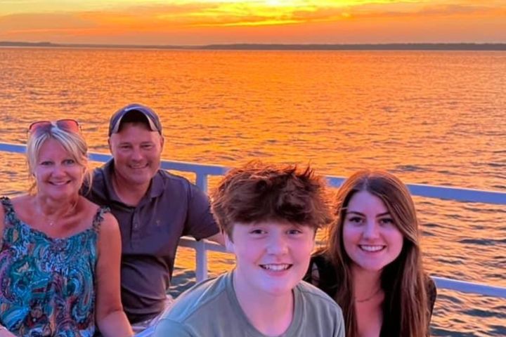 Group of four people smiling on a boat at sunset with water backdrop.