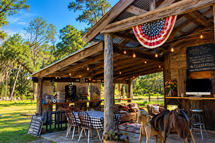 Rustic outdoor pavilion with wooden beams, American flag, tables, chairs, and greenery.