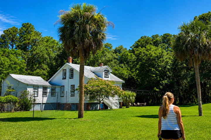 Person walking toward a white house with palm trees and a lush lawn.