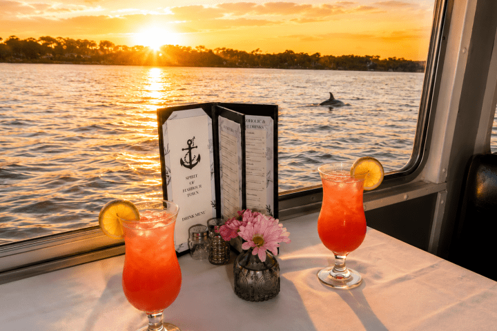 Two cocktails on a table by a window with a sunset view over water.
