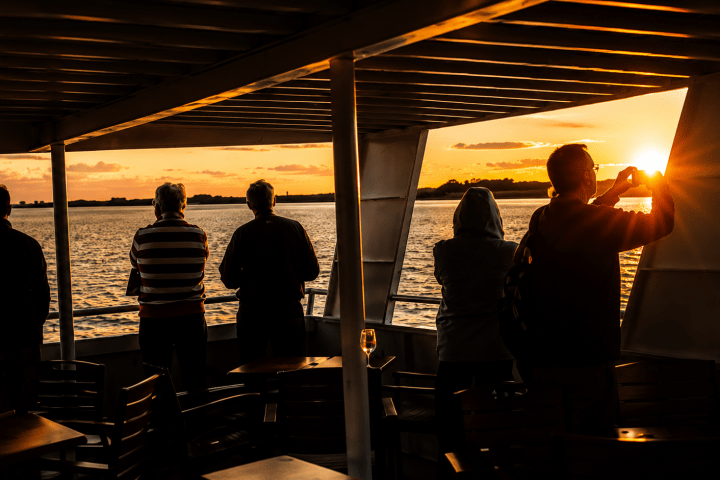 Five people on a boat watching a sunset over the water.