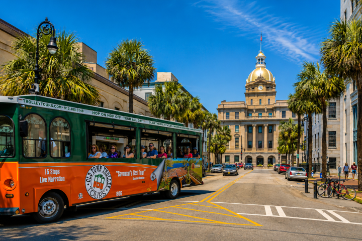 Tourist trolley on street with palm trees and historic building in background.