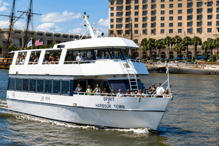 White ferry boat on water with passengers, city buildings in background.