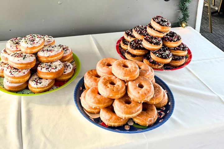 Three piles of donuts on colorful plates on a white tablecloth.