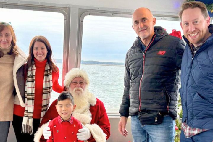 Group photo with a young child and Santa on a boat with a sea view.