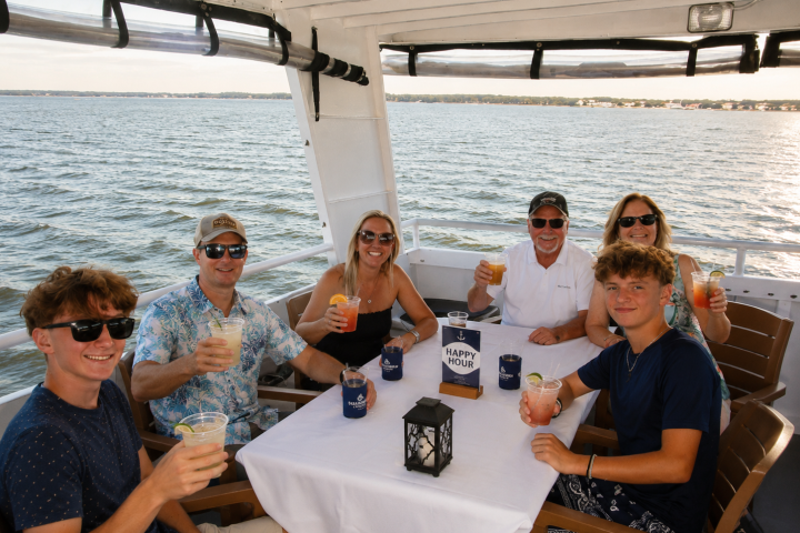 Six people enjoying drinks at a table on a boat with ocean view.
