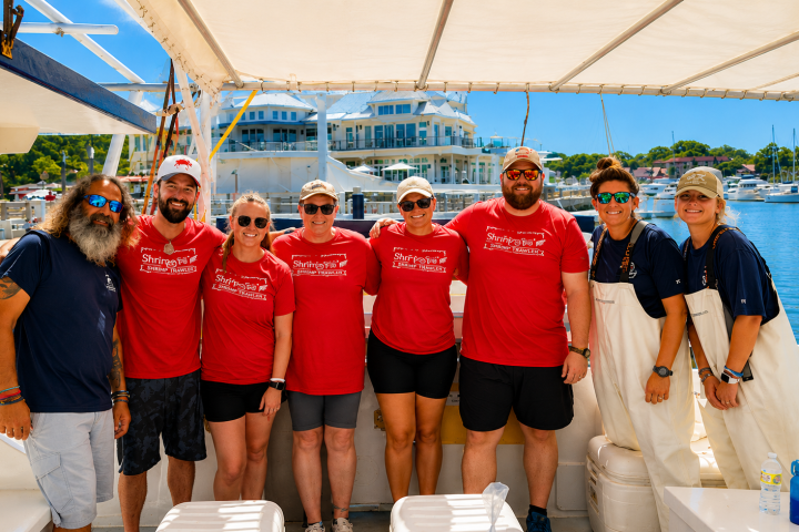 Group of people in red shirts on a boat with marina background.