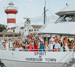 Group of people on a boat named Spirit of Harbour Town, with a red and white lighthouse in the background.