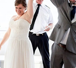 Bride in white dress and groom in gray suit dancing joyfully.