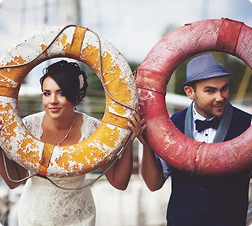 Bride and groom holding lifebuoys, smiling outdoors.