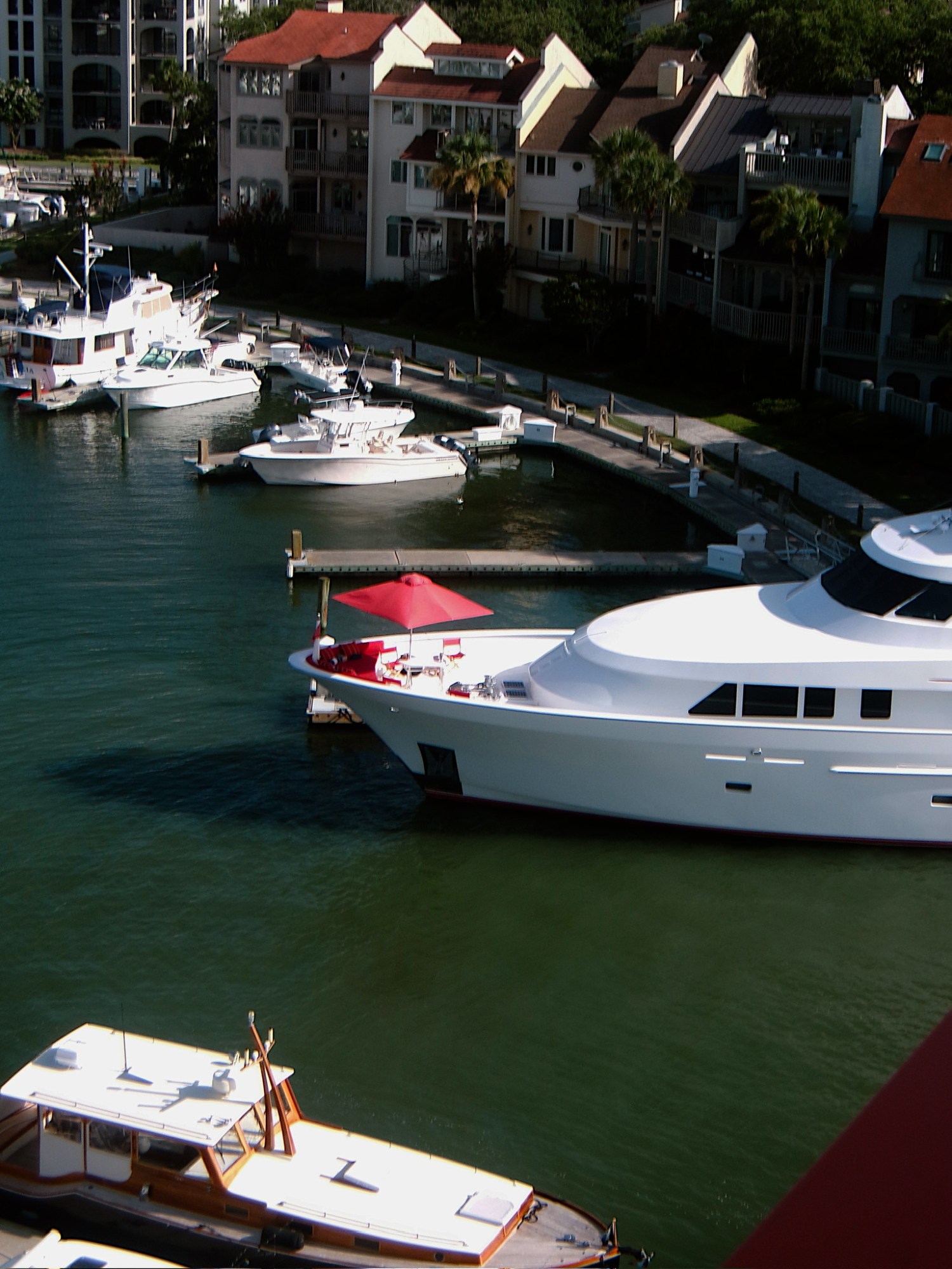 Boats docked at a marina, with a large white yacht and red umbrella visible.