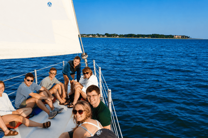 Group of people relaxing on a sailboat in calm blue water.