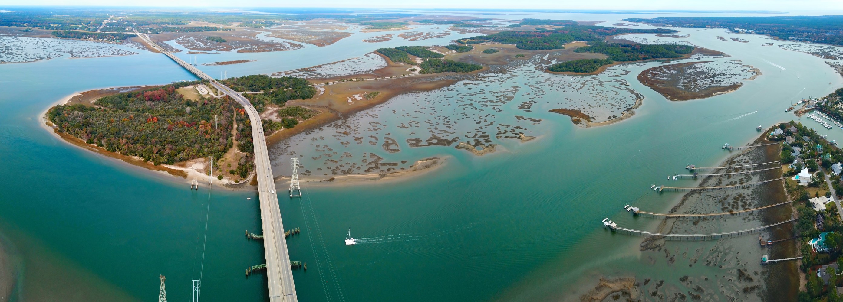 Panoramic view of a bridge over water with islands and boats docked along the shore.