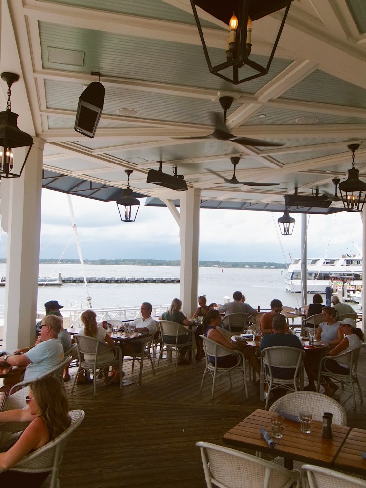 People dining on a covered outdoor patio overlooking a marina.