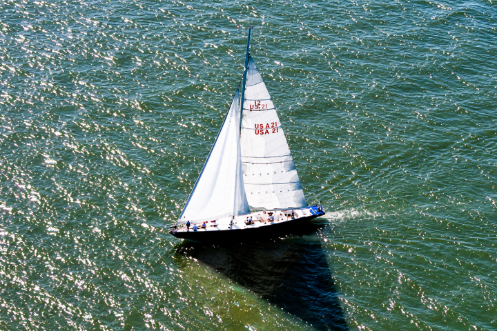 Sailboat with white sails cutting through green water on a sunny day.