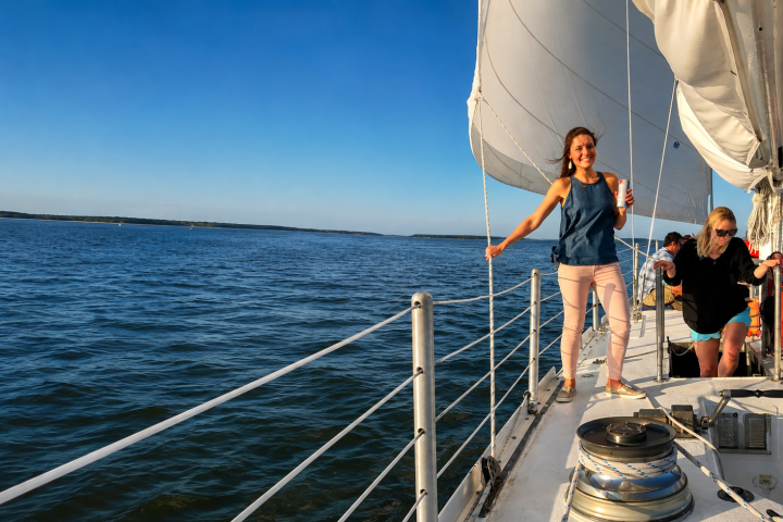 People on a sailboat with white sails, relaxing on a sunny day.