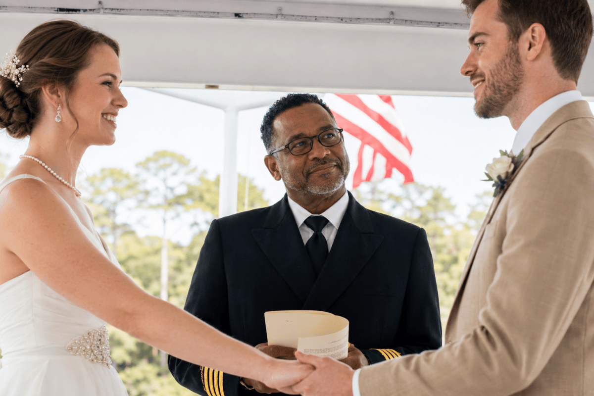 Bride and groom holding hands, smiling at each other, with officiant in the background.