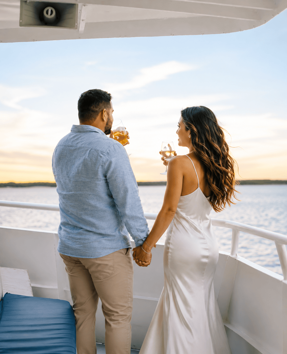 Couple holding hands on a boat, enjoying drinks at sunset.